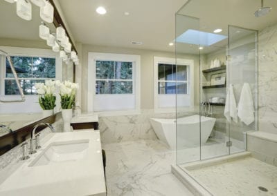 marble, white-tiled bathroom, with a glass wall shower, dim lights and two white basins